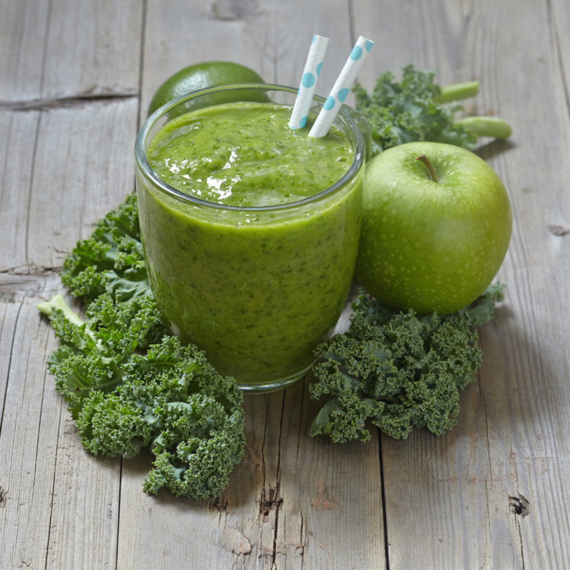 image of apple-kale smoothie surrounded by leafy kale and green apples on light wood table