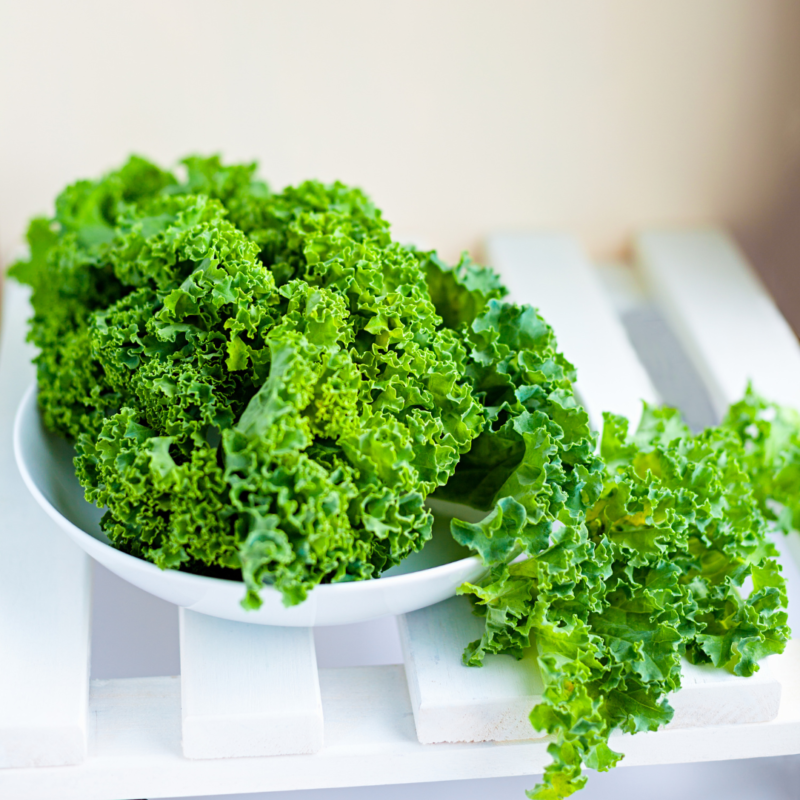 Image of bright, fresh kale in white bowl atop a slatted white table