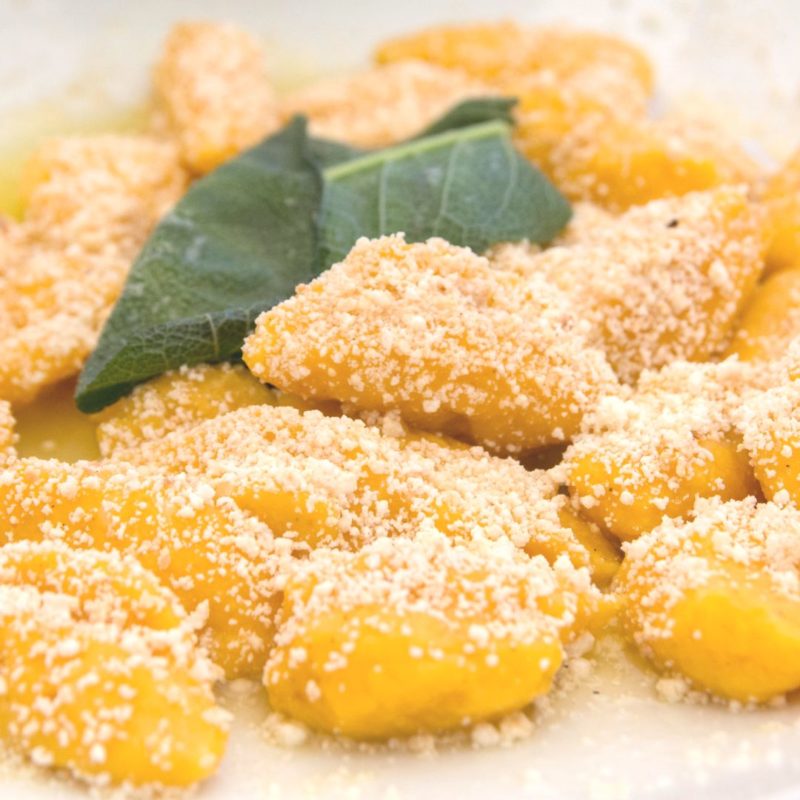Close-up image of pumpkin gnocchi with a sage leaf, sprinkled with grated Parmigiano Reggiano ppma