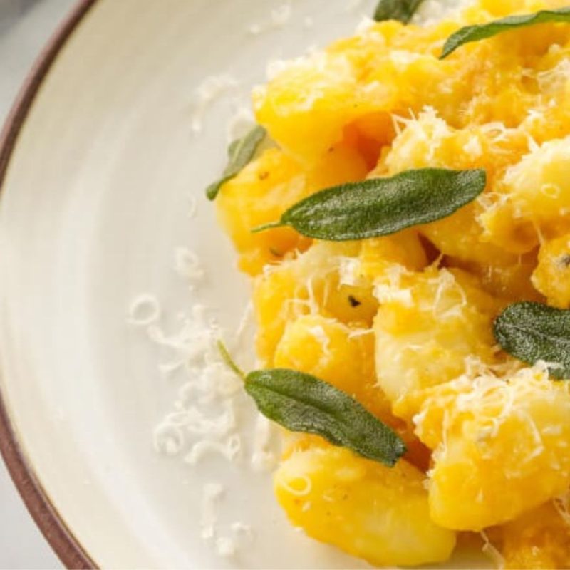 Image shows a white plate with a serving of pumpkin gnocchi with grated Parmigiano Reggiano and fresh sage from healthy recipe ppma