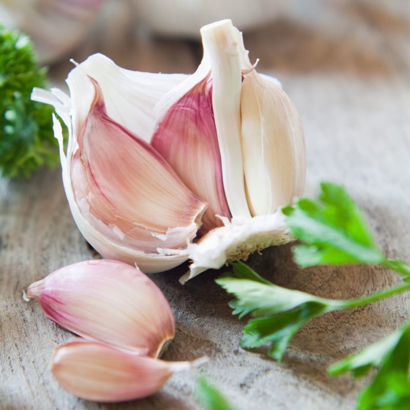 Image of raw garlic bulb open into cloves with several parsley leaves nearby for healthy recipe nutritionist PPMA
