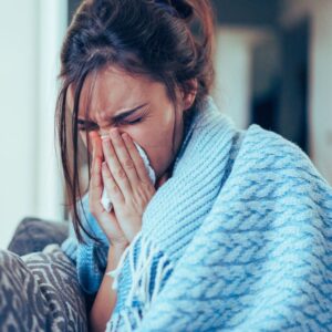 Image of woman wrapped in a blanket blowing her nose sick with a cold ppma private physicians medical associates