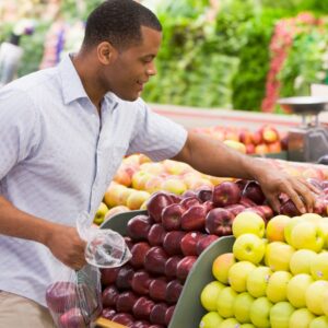 Image of young man selecting apples at a grocery store or supermarket for eating healthy on a budget PPMA private physicians medical associates