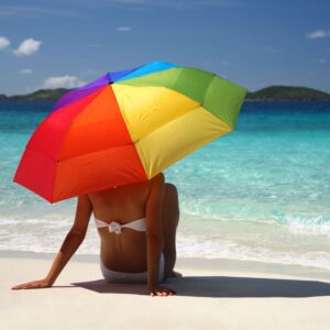 Woman sitting under colorful umbrella at the shore. PPMA. private physicians medical associates
