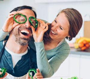 Couple laughing while preparing a healthy meal in the kitchen, woman placing green pepper slices over man's face, like glasses. Nutrition for Eye Health Author: Romana Brennan MS RD PPMA Private Physicians Medical Associates Concierge Medicine, Newport Beach, California