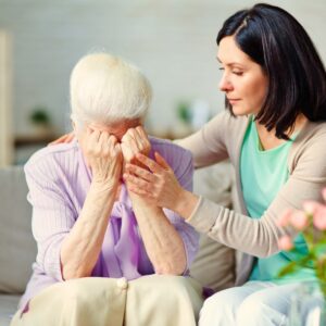 Image of senior woman with white hair and hands covering her face being comforted by a younger dark-haired woman. Grief and depression. Private Physicians Medical Associates PPMA