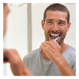Image of handsome young bearded man smiling as he brushes his teeth in the bathroom mirror. quick tips for health. PPMA. private physicians medical associates