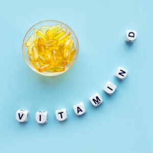 The image shows a clear glass bowl with yellow translucent supplements on a blue surface, with the words "VITAMIN D" spelled out in blocks. The Importance of Vitamin D. PPMA. Private Physicians Medical Associates