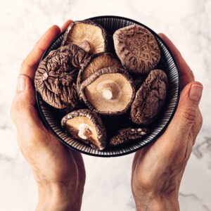 Image shows a person's hands holding a round bowl filled with dried Shitake mushrooms over a white marble counter. Mushrooms nutritious and delicious. Private Physicians Medical Associates. PPMA.