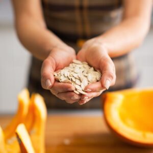 Image of a person holding raw pumpkin seeds in their cupped hands, with sliced pumpkin pieces nearby. PPMA Private PHysicians Medical Associates