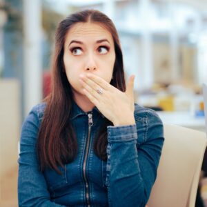 Image shows a young woman dressed in denim holding her hand over her mouth, suppressing a burp. Stomach ulcers – what to know. Private Physicians Medical Associates. PPMA. Concierge Medicine. Newport Beach CA.