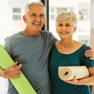 An image of a middle-aged couple, male and female, each holding a yoga mat and smiling.