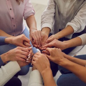 This image shows the hands of six people who are holding hands together in the center of a circle to show emotional support. For A Fresh Start in the new year.