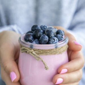 This image shows a pink jar of blueberries with jute wrapped around the top - all being held by two hands with pink polish on the nails.