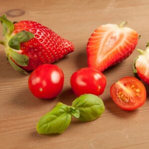 Am image of several strawberries and cherry tomatoes with a garnish of basil