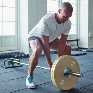 An image of a middle aged or senior man lifting a weight at the gym. Weightlifting.