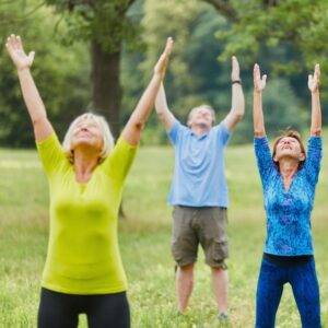 A group of three seniors/middle-aged people stretching, doing Tai chi in a park.