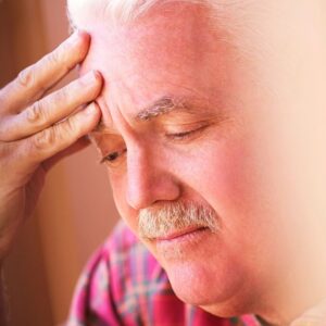 An image of a middle aged or senior man with his fingers on his forehead as he looks down, sad or depressed.