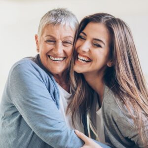 An image of a middle-aged mother and her daughter embracing and laughing. Aging.