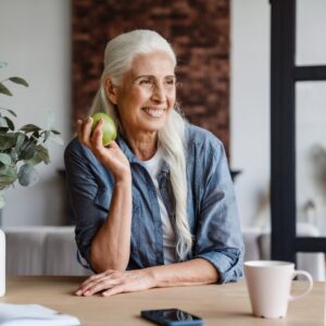 An image of a middle-aged or senior woman smiling as she holds a green apple in her hand.
