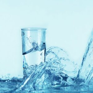 A blue-hued image of a glass of water with water splashing around it. Hydration
