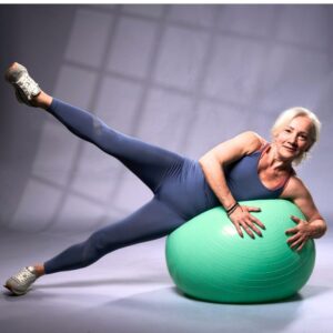Am image of a middle-aged or senior woman exercising with a teal exercise ball. Fitness age.