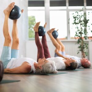 An image of middle-aged people in an exercise class, on their backs lifting balls between their feet.