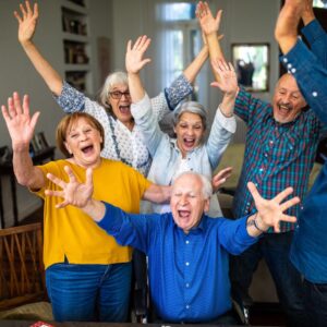 A group of middle-aged and senior adults celebrating, their arms in the air, laughing and smiling.