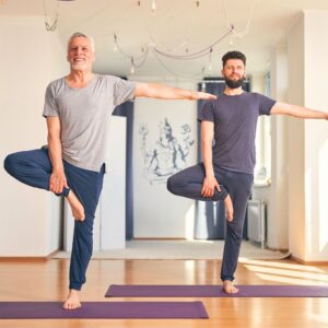 An image of an older man and a younger man practicing balance through yoga.