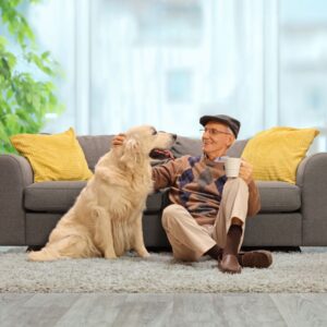 An image of a senior or middle-aged man dressed in a dapper outfit, sitting on his living room floor with his large honey-colored dog. Friendship and the art of aging well.