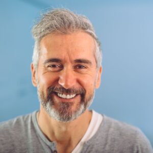 An image of a handsome middle-aged man with silver hair and beard smiling into the camera.