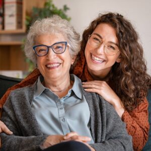 Image of a senior woman and her granddaughter, both seated and smiling.