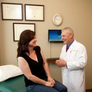 An image of a woman patient sitting atop the exam table as she talks with a smiling Dr. Van Meter.