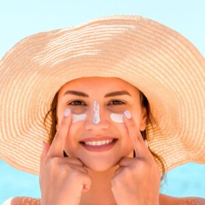 An image of a smiling woman wearing a straw hat and white suntan lotion for SPF protection on her face. Summer Road Trip Guide: Healthy Travel Tips