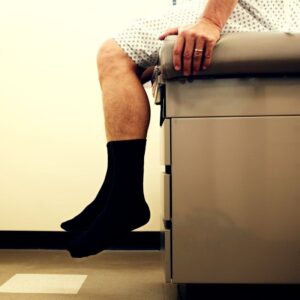 An image showing the bottom half of a patient sitting on an exam table at the doctor's office, wearing black socks. Empowering Well-being: Personalized Concierge Healthcare