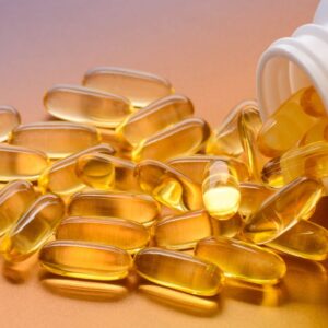 Close-up image of amber-colored vitamin d capsules spilling from a white bottle.