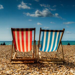 Summertime image showing two striped beach chairs - one red and white, the other blue and white - with the shore, ocean, and blue sky beyond. Sunscreen and Vitamin D