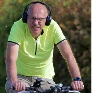 An image of a middle-aged man wearing headphones and glasses as he rides his bicycle.