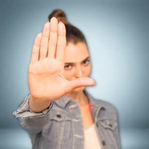 An image of a woman wearing a white shirt and denim jacket, her right arm outstretched, holding her right hand in a
