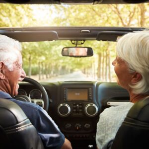An image of a couple driving along a lane of trees, smiling at each other.