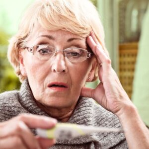 An image of a senior woman or middle-aged woman checking her temperature and looking stunned at the thermometer