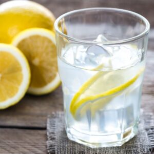 An image of a glass of ice water with lemon slices and a lemon with slices to the side of it. Hydration
