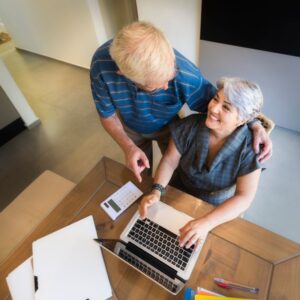 An image of a couple planning together, the woman seated at a laptop and the man hugging her from behind.