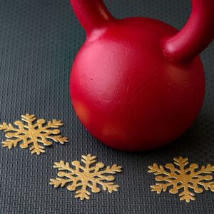 An image of a red kettle ball with three large gold star decorations on the floor around them. Stay active during the holiday season
