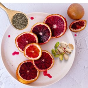 A plate with slices of blood orange, pistachios and a wooden spoonful of chia seeds