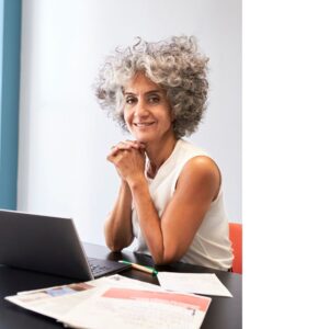Image of a middle-aged woman sitting at her desk researching info regarding her health-related bad news, smiling into the camera.