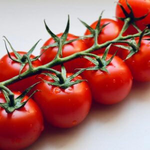 A close-up image of cherry tomatoes still on the vine, with a gray/white background