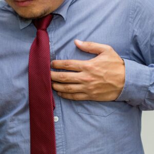 A person wearing a blue shirt and maroon tie clutches their chest, as if having heart disease symptoms.