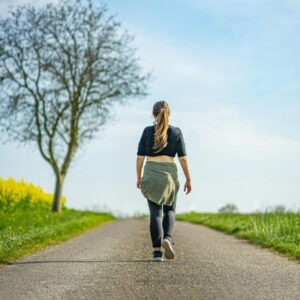 Woman walking away on road with blue sky
