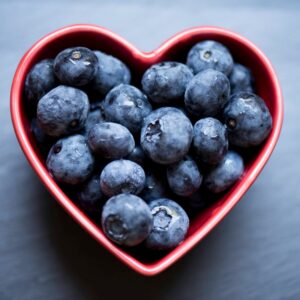Blueberries in a deep red heart-shaped bowl.